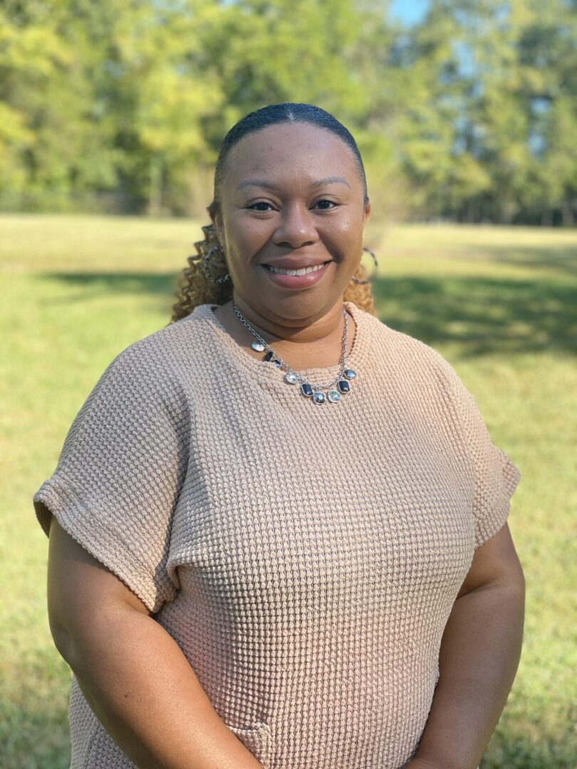 A woman standing in the grass wearing a tan shirt.