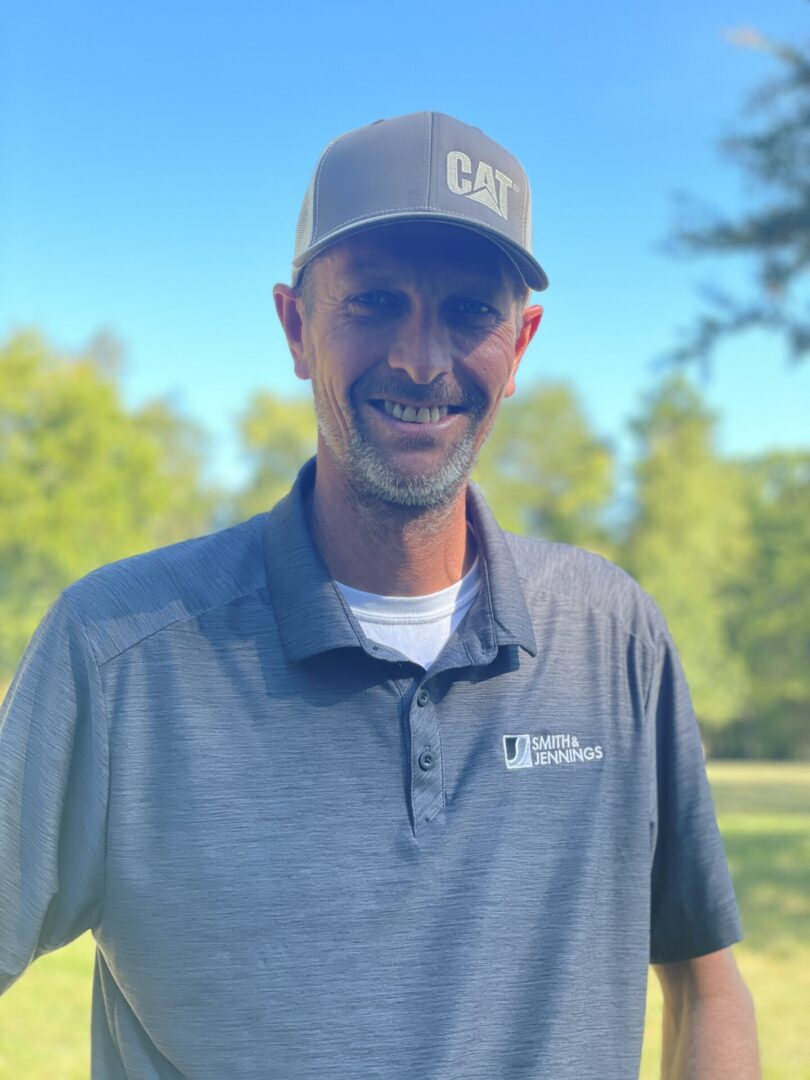 A man wearing a hat standing in front of trees.